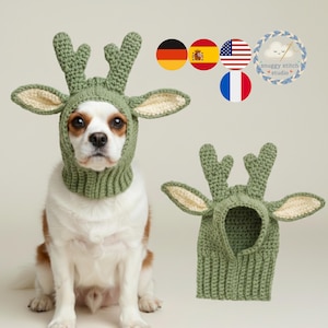 Könnte beinhalten: Ein Hund trägt eine grüne gehäkelte Rentier-Mütze mit cremefarbenen Ohren und Geweih. Der Hund ist weiß und braun. Eine zweite Mütze wird neben dem Hund gezeigt. Das Logo von Snuggy Stitch Studio befindet sich oben rechts.