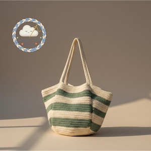 Op de afbeelding: Een crèmekleurige, gehaakte draagtas met horizontale strepen in gedempt groen. De tas heeft twee lange handvatten en een afgeronde bodem. De tas is handgemaakt. Een logo met een wolk en tekst staat in de linkerbovenhoek.
