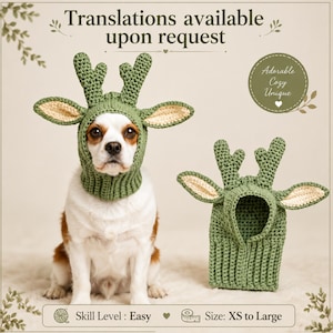 May include: A sage green crocheted pet hat featuring two upright antlers and two wide, pointed ears with cream-coloured inner detailing. The hat has a ribbed neck section and is shown on a dog, with a second identical hat placed beside it.