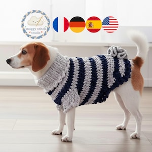 May include: A dog wearing a handmade, gray and navy blue striped crochet sweater. The sweater has a high collar and a decorative flower detail on the back. The dog is a Beagle mix, standing on a light wood floor.