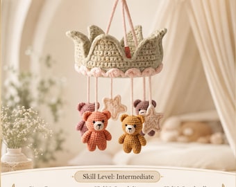 May include: A crochet baby mobile featuring a sage green crown base with a light pink scalloped trim. Hanging from the crown are four small stuffed bears in shades of brown and pink, along with two cream-colored stars. The crown is 8 inches in diameter and 5 inches tall, while the animals are 3.75 inches tall.