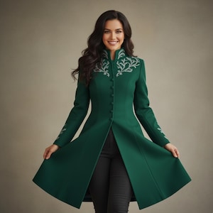 May include: A long, emerald green coat with a high collar and silver embroidered detailing. The coat features a button-down front and flared skirt. The sleeves also have silver embroidery. The person in the image is wearing black pants.