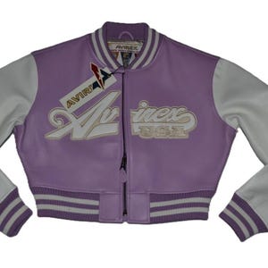 Può includere: Giacca college Avirex USA lavanda e bianca. La giacca presenta maniche bianche, una cerniera nera e il logo Avirex in bianco. I polsini e il colletto hanno strisce bianche e lavanda.