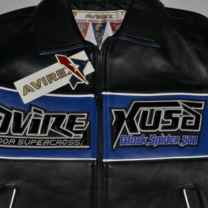 Puede incluir: Chaqueta de cuero negra con detalles azules y blancos. Presenta la marca "AVIREX" y los textos "INDOOR SUPERCROSS" y "Black Spider 500". Incluye cierre de cremallera y etiqueta.