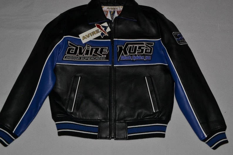 Puede incluir: Chaqueta de cuero negra con detalles azules y blancos. Presenta el texto "AVIRE Indoor Supercross" y "XUSA Black Spider 500". Incluye cierre de cremallera, bolsillos y pu&ntilde;os y dobladillo acanalados.