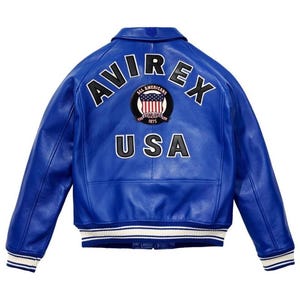 May include: A bright blue leather jacket featuring the word "AVIREX" arched across the shoulders. Below, the word "USA" is displayed. A circular patch with the words "ALL AMERICANS ESTABLISHED 1975" and a US flag design is centered. The jacket has white and blue striped cuffs.