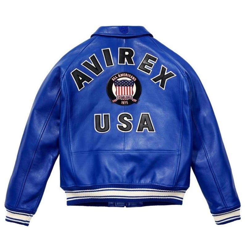 May include: A bright blue leather jacket featuring the word "AVIREX" arched across the shoulders. Below, the word "USA" is displayed. A circular patch with the words "ALL AMERICANS ESTABLISHED 1975" and a US flag design is centered. The jacket has white and blue striped cuffs.