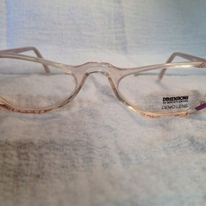 May include: Clear plastic eyeglasses with a pink and purple trim. The glasses have a 'DIMENSIONS by SoChic Optics DEMO LENS' label on the right lens.