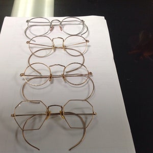 May include: Four pairs of eyeglasses with different frame styles and colors. The top pair is silver, the second pair is gold, the third pair is gold, and the bottom pair is gold with a unique octagonal shape.