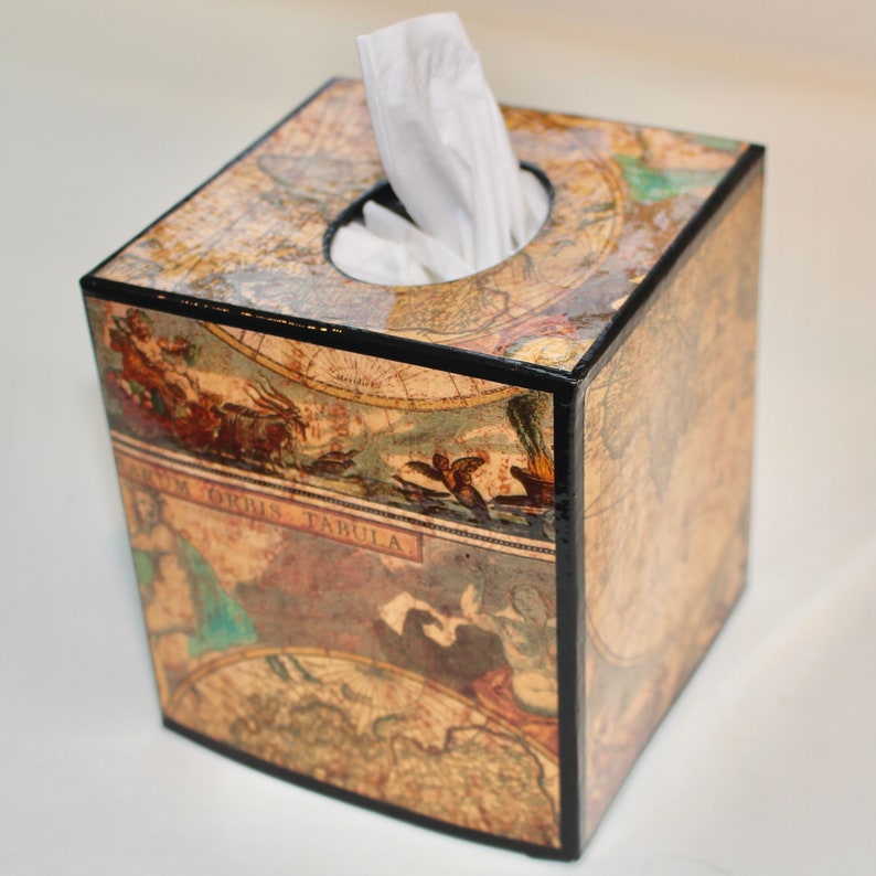May include: Square tissue box featuring a vintage map design with a black trim. The box has a circular opening at the top for tissue dispensing. The map design includes illustrations and text, adding a classic aesthetic.