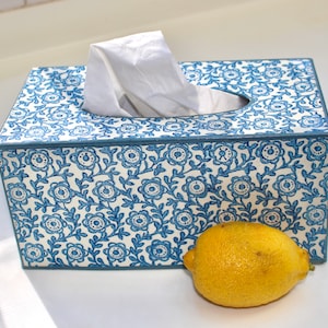 May include: A blue and white floral patterned tissue box with a white tissue inside and a yellow lemon in front of it.