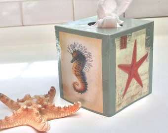 May include: A light blue tissue box cover with a seahorse and starfish design. The box has a white tissue dispenser on top.