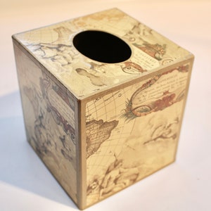 May include: A square tissue box cover with a vintage world map design. The cover is made of wood and has a cream background with brown and black details. The map features text in French and Latin.