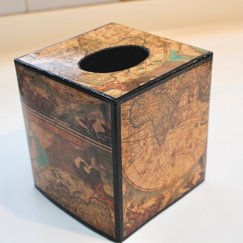 May include: A square tissue box featuring a vintage world map design. The box has a black trim and a dark oval opening on top. The map design is in shades of brown, beige, and blue.