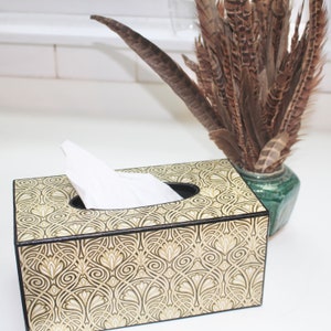 May include: A decorative tissue box cover with a black and gold geometric pattern. The cover is made of wood and has a rectangular shape.