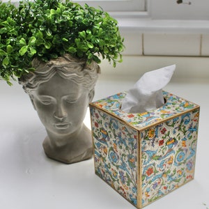 May include: A decorative tissue box cover with a floral pattern in shades of blue, green, and gold. The cover is made of wood and has a white tissue box inside.