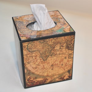 May include: A square tissue box with a vintage world map design. The box is brown with black trim and a circular opening at the top. White tissues are visible. The map features continents and nautical details.