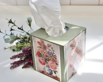 Könnte beinhalten: Ein quadratischer Taschentuchspender mit hellgrüner Lackierung. Er zeigt ein Blumendesign mit rosa, roten und blauen Blumen. Weiße Taschentücher ragen aus der Öffnung. Ein Strauß lila und grüner Blumen liegt daneben.
