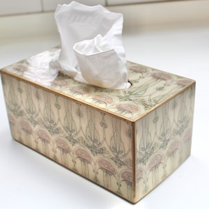 May include: A tissue box cover with a floral design in shades of pink, green, and cream. The box is made of wood and has a gold trim.