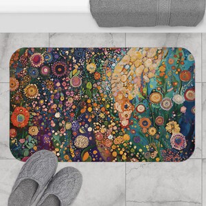 May include: A rectangular bath mat with a colorful floral design. The mat features a vibrant array of flowers in shades of orange, yellow, blue, and purple against a dark background. The mat is placed on a tiled floor, with a pair of gray slippers in the foreground.