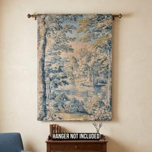 May include: A rectangular wall tapestry featuring a woven landscape scene with trees, foliage, and a body of water in shades of blue, beige, and cream. The tapestry hangs from a metal rod. The text HANGER NOT INCLUDED is visible below.
