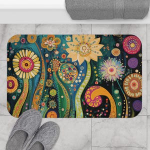 May include: A rectangular bath mat with a vibrant floral design. The mat features large yellow and pink flowers, green stems, and a dark teal background. The design includes various colorful dots and swirls, creating a whimsical and artistic look. Gray slippers are at the bottom.