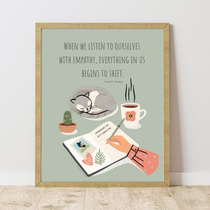 Può includere: Una stampa artistica incorniciata con sfondo verde chiaro. La stampa presenta un gatto grigio che dorme, un cactus, una tazza di caffè e un diario con la scritta "JOURNALING FOR SELF-CONNECTION". La citazione "WHEN WE LISTEN TO OURSELVES WITH EMPATHY, EVERYTHING IN US BEGINS TO SHIFT" è in alto.