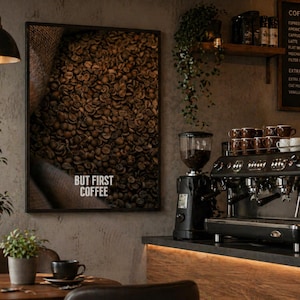 Peut inclure: Une affiche encadrée montrant des grains de café sortant d'un sac en toile de jute. Le texte "BUT FIRST COFFEE" est imprimé en blanc. Une machine à expresso noire, un moulin et des tasses à café sont visibles.