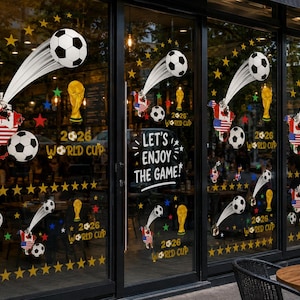 May include: Window decals featuring soccer balls in motion, maps of North America with national flags, gold trophy icons, and yellow stars. The text reads 2026 WORLD CUP and LET'S ENJOY THE GAME. These decorative stickers are applied to glass panels.