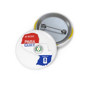 May include: Two round pin-back buttons featuring a white background. One button displays a map of Paraguay colored in red, white, and blue with the text WE BELIEVE PARAGUAY, the national coat of arms, and the text ROUND OF 16 with a trophy icon.