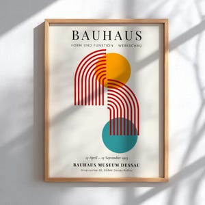 Pode incluir: Impressão artística Bauhaus emoldurada com formas geométricas em vermelho, amarelo e turquesa. O texto inclui "BAUHAUS" e "FORM UND FUNKTION - WERKSCHAU". Inclui também datas e o endereço do Bauhaus Museum Dessau. A moldura é de cor castanho claro.