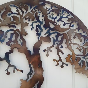May include: A metal wall art sculpture of a tree with a brown and blue patina finish. The tree is cut out of the metal and has a detailed design.