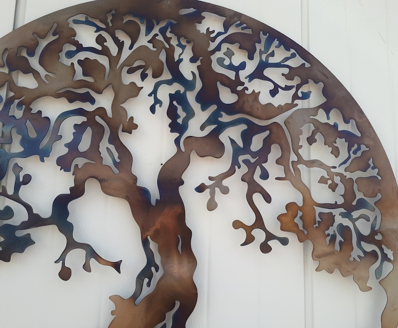 May include: A metal wall art sculpture of a tree with a brown and blue patina finish. The tree is cut out of the metal and has a detailed design.