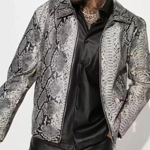 May include: A gray and white snakeskin-patterned leather jacket with a zipper closure. The jacket is worn over a black button-up shirt. The text "FIELD LEATHER" is visible at the top left.