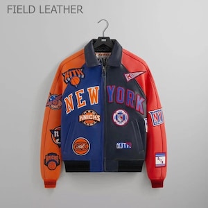 Puede incluir: Chaqueta de cuero de dos tonos con paneles naranjas, azules y rojos. La chaqueta presenta las palabras "NEW YORK" y varios parches de equipo. Las mangas son naranjas y el cuerpo est&aacute; dividido entre azul y negro. La chaqueta est&aacute; colgada de una percha negra.
