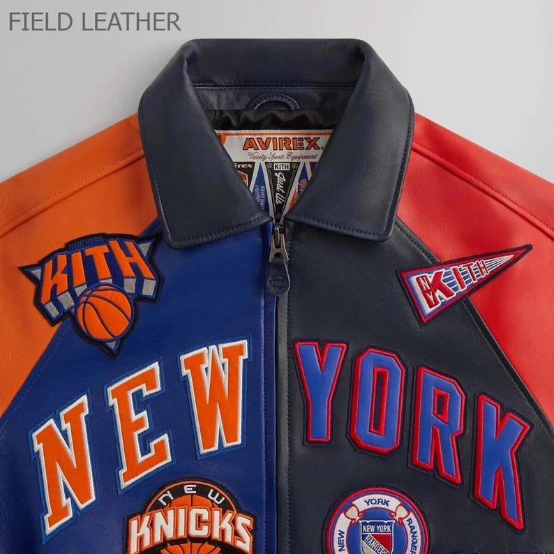 Puede incluir: Chaqueta de cuero con bloques de color en paneles naranja, azul, negro y rojo. La chaqueta presenta el texto "NEW YORK" y "KNICKS" con logotipos de baloncesto y del equipo. El cuello es azul marino y la chaqueta tiene cierre de cremallera.