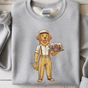 May include: A light gray sweatshirt featuring a cartoon Golden Retriever wearing a white shirt, tan pants, and a cap, holding a tray with three mugs of beer. The dog has brown suspenders. The sweatshirt has a crew neck.