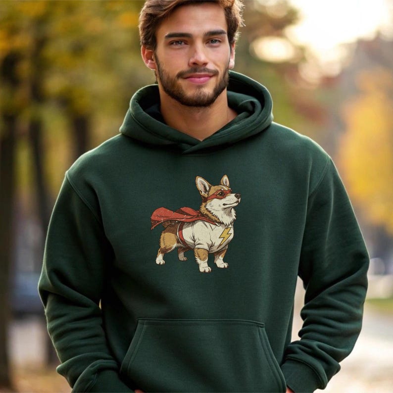 May include: A dark forest green hooded sweatshirt featuring a graphic print of a Corgi dog dressed as a superhero. The dog wears a red cape, a red eye mask, and a white shirt with a yellow lightning bolt emblem on the chest area.