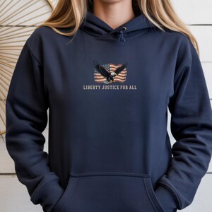 May include: Navy blue hoodie with a front graphic featuring an American flag, an eagle, and the text "LIBERTY JUSTICE FOR ALL". The hoodie has a drawstring hood and a front pocket.