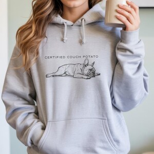 May include: A light gray hoodie with a front pocket and drawstring hood. The hoodie features a black and white illustration of a French Bulldog lying down, with the text "CERTIFIED COUCH POTATO" above the dog.