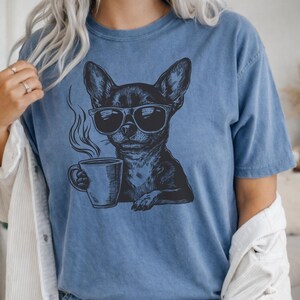 Puede incluir: Camiseta azul con un gr&aacute;fico negro de un chihuahua con gafas de sol y una taza de caf&eacute;. El perro est&aacute; representado con vapor saliendo de la taza. La camiseta tiene un corte holgado y cuello redondo.