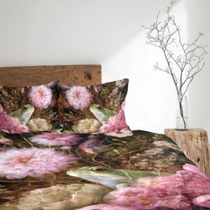 May include: A bedding set featuring a dark brown background with a repeating pattern of light green frogs and large, soft pink dahlia flowers. The design includes two matching pillowcases and a duvet cover, all displaying the same botanical and amphibian motif.