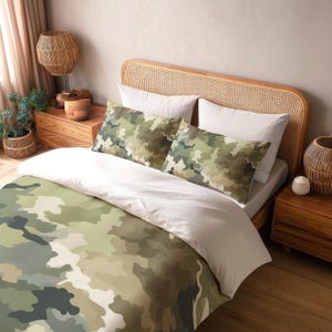 Peut inclure: Une parure de lit comprenant une housse de couette et deux taies d'oreiller avec un motif camouflage dans des tons vert olive, sauge, vert forêt foncé et crème. La literie est présentée sur un lit avec un matelas clair et des oreillers blancs.