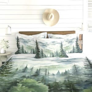 Può includere: Un set da letto con stampa ad acquerello di una foresta nebbiosa con alti pini nelle tonalità del verde, grigio e bianco. Il set include una trapunta e due federe abbinate, che mostrano un paesaggio continuo di alberi sempreverdi.