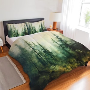 May include: A bedding set featuring a duvet cover and two pillowcases with a printed forest scene. The design displays tall evergreen trees in shades of dark green and muted sage against a light, misty background, creating a layered effect.