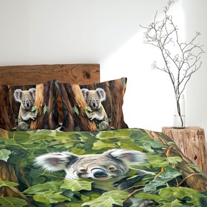 Op de afbeelding: Dekbedovertrekset met een gedetailleerde illustratie van koala's in een naturalistische omgeving. De set bevat twee kussenslopen met koala's in bomen en een dekbedovertrek met een koala tussen groen gebladerte. Het kleurenpalet omvat groen, bruin en grijs.