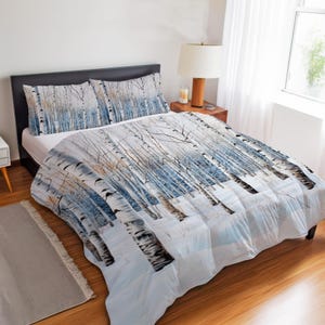 May include: A bedding set featuring a printed pattern of a winter forest with white birch trees, bare branches, and blue-toned shadows on a snowy ground. The set includes a comforter and two matching pillow shams, all displaying the same continuous woodland scene.