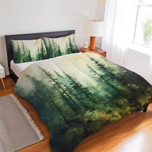May include: A bedding set featuring a duvet cover and two pillowcases with a printed forest scene. The design displays tall, dark green pine trees fading into a misty, light-colored background, creating a continuous landscape across the bed.