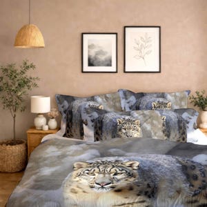 May include: A bedding set featuring a snow leopard design. The duvet cover and pillowcases display a detailed image of a snow leopard with a snowy mountain backdrop. The color palette includes shades of gray, white, and beige.