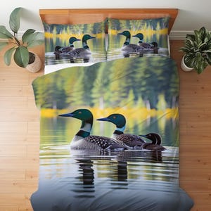 May include: A bedding set featuring a duvet cover and two pillowcases with a photographic print of common loons swimming on a calm lake. The scene depicts adult loons with black and white speckled plumage and dark heads, accompanied by a small chick.